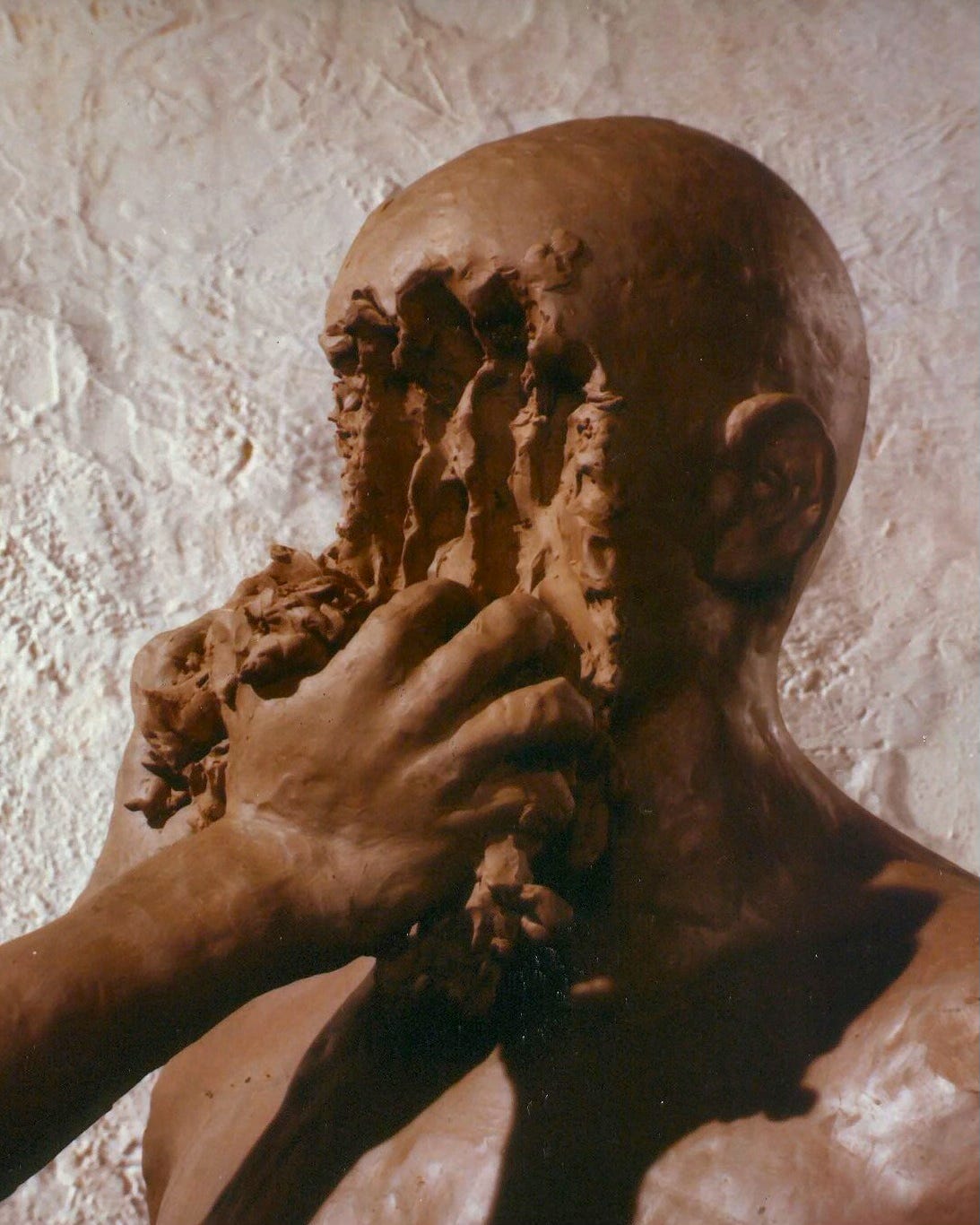 A clay figure has its face literally scraped off by someone else's hand.