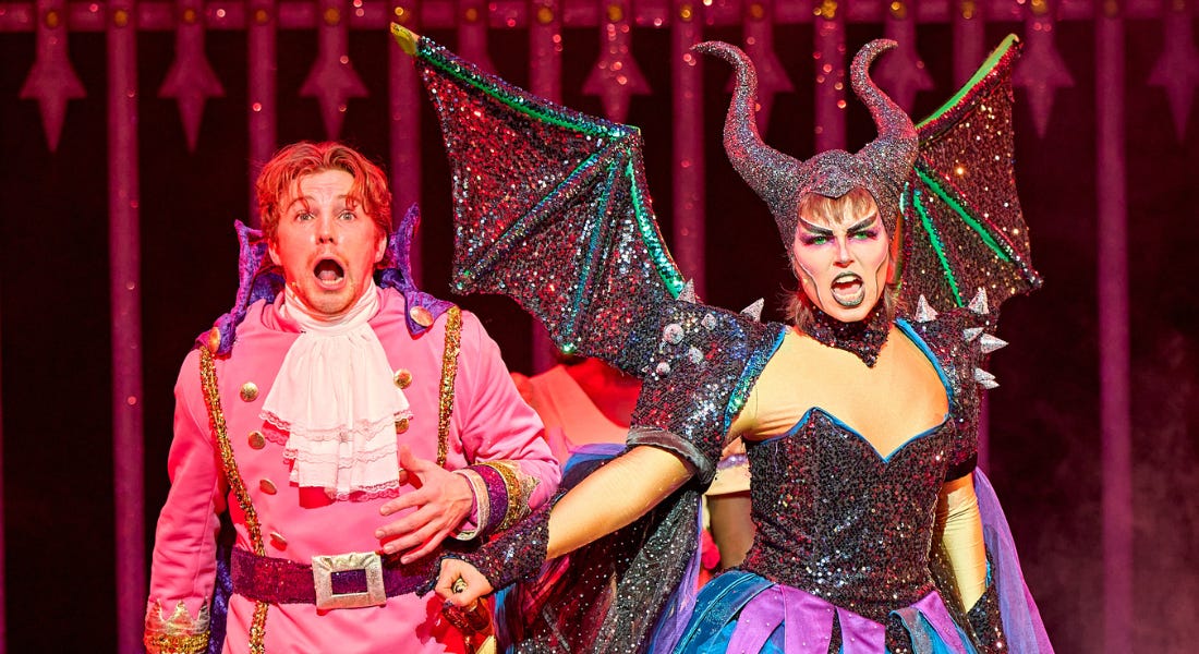 A man is standing upright wearing a regal pink and purple jacket, shirt and trousers, his mouth is wide open with complete shock. A person is standing next to him wearing a black, purple and blue sparkly dress, they have large glittery wings and black horns extending from their head. They have their right hand tightly clasped around the man’s sword, which is attached to his waist band. A man is standing upright wearing a regal pink and purple jacket, shirt and trousers, his mouth is wide open with complete shock. A person is standing next to him wearing a black, purple and blue sparkly dress, they have large glittery wings and black horns extending from their head. They have their right hand tightly clasped around the man’s sword, which is attached to his waist band.