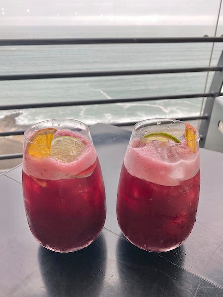 Moradita cocktail with purple corn and pisco in front of a view of Costa Verde