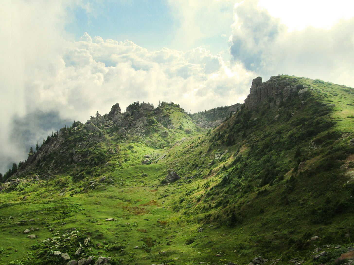 image of green, rocky sloping hill with clouds in the background, could be Ireland