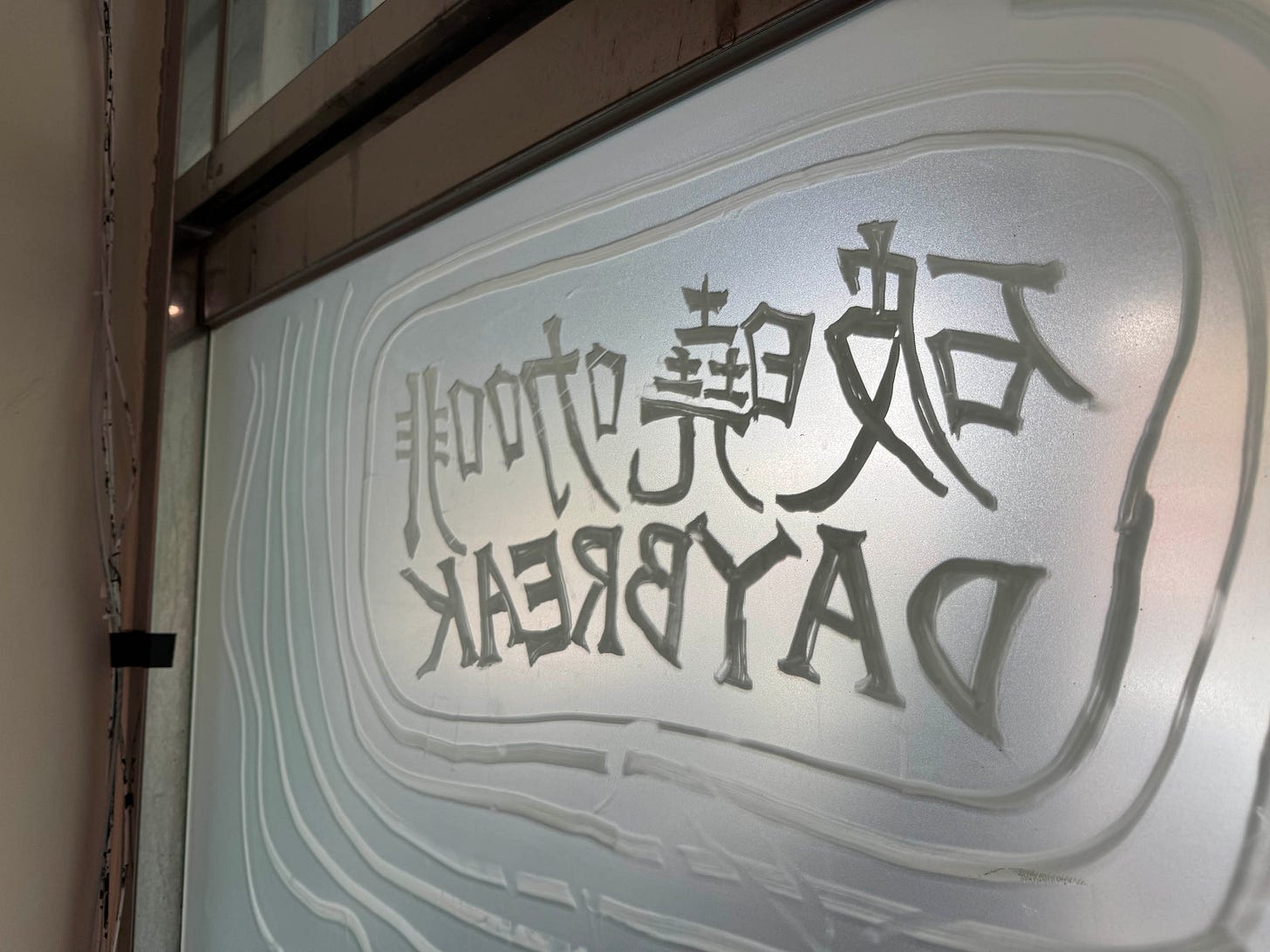 Horizontal photo of a closeup inside view of the glass door at Daybreak in Wanhua. The hand-drawn etching on the glass reads Daybreak Cafe in both English and Traditional Chinese, mirrored.