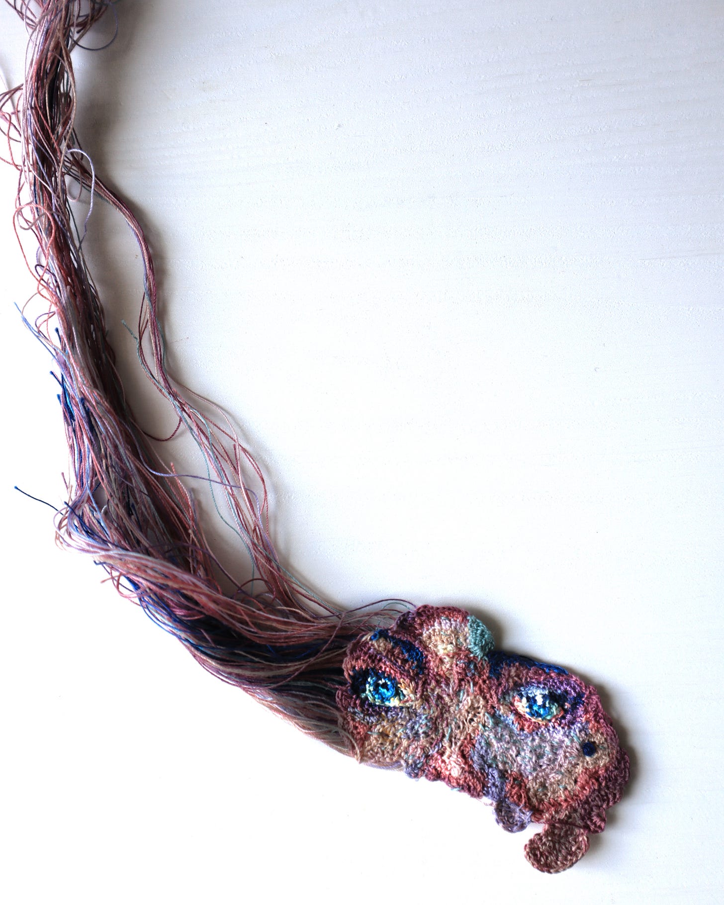 Part of a crochet portrait lays flat on a white table. Threads still attached to the portrait spread upwards over it.