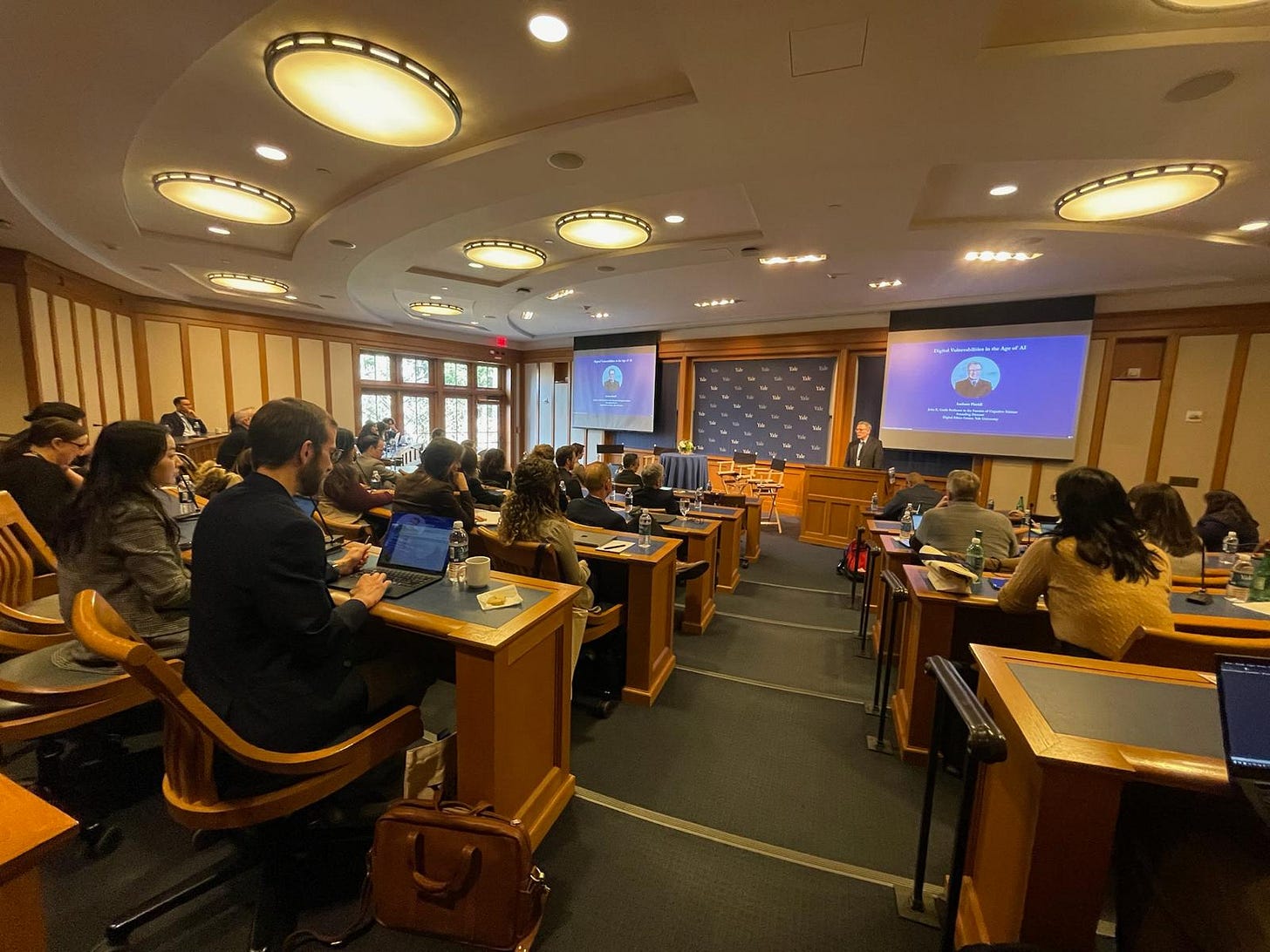A man speaking in front of a full audience in a lecture hall.