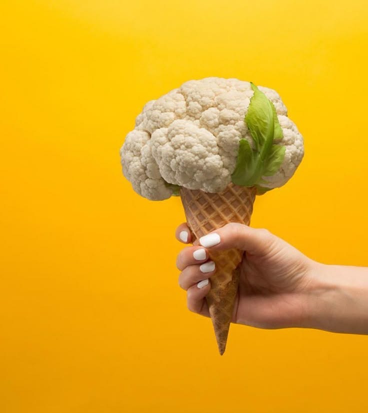 This may contain: a hand holding an ice cream cone with cauliflower on it, against a yellow background This may contain: a hand holding an ice cream cone with cauliflower on it, against a yellow background