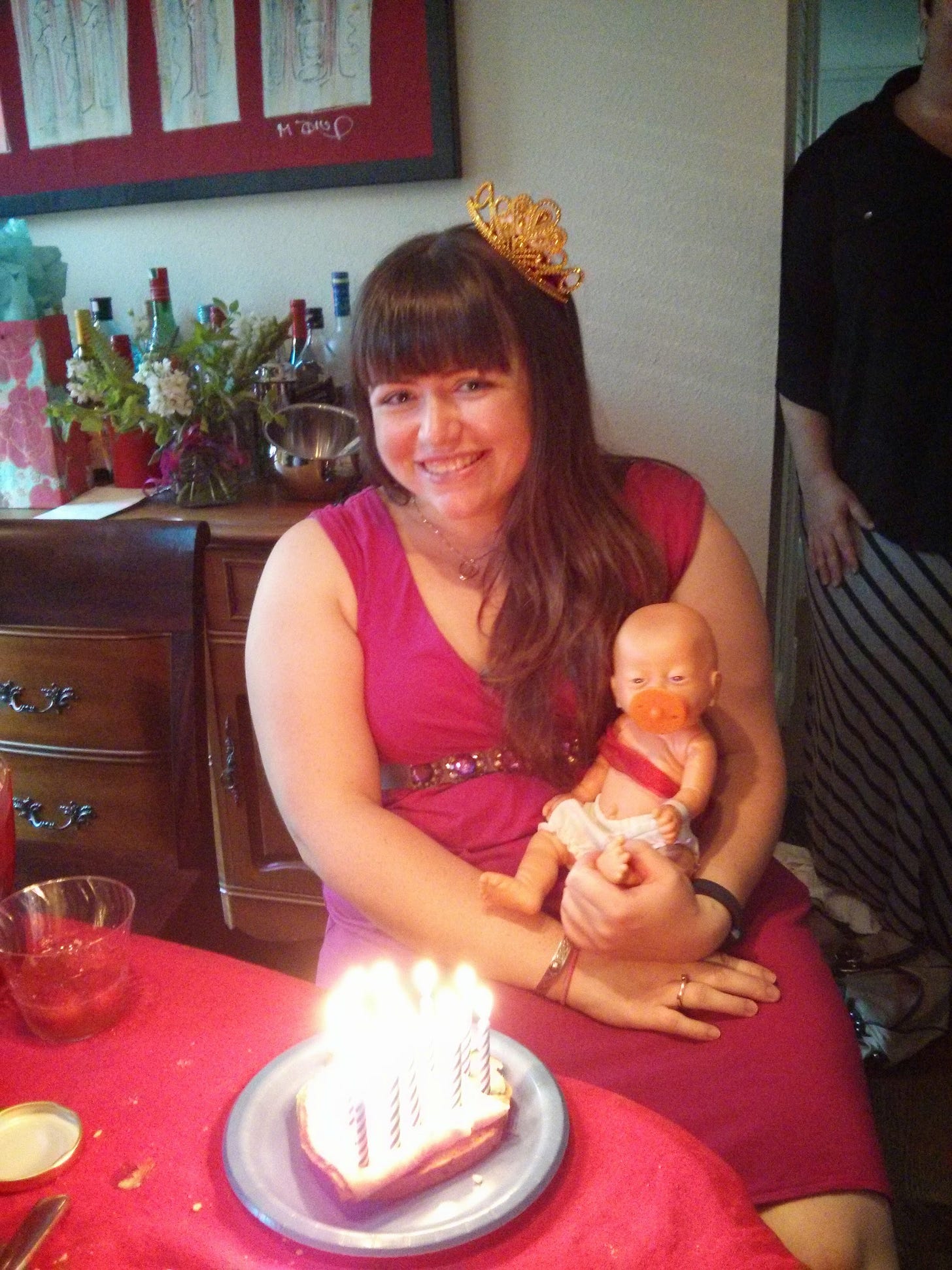 Photo of the author wearing a pink dress and a small fake crown, holding a fake baby. Photo of the author wearing a pink dress and a small fake crown, holding a fake baby.