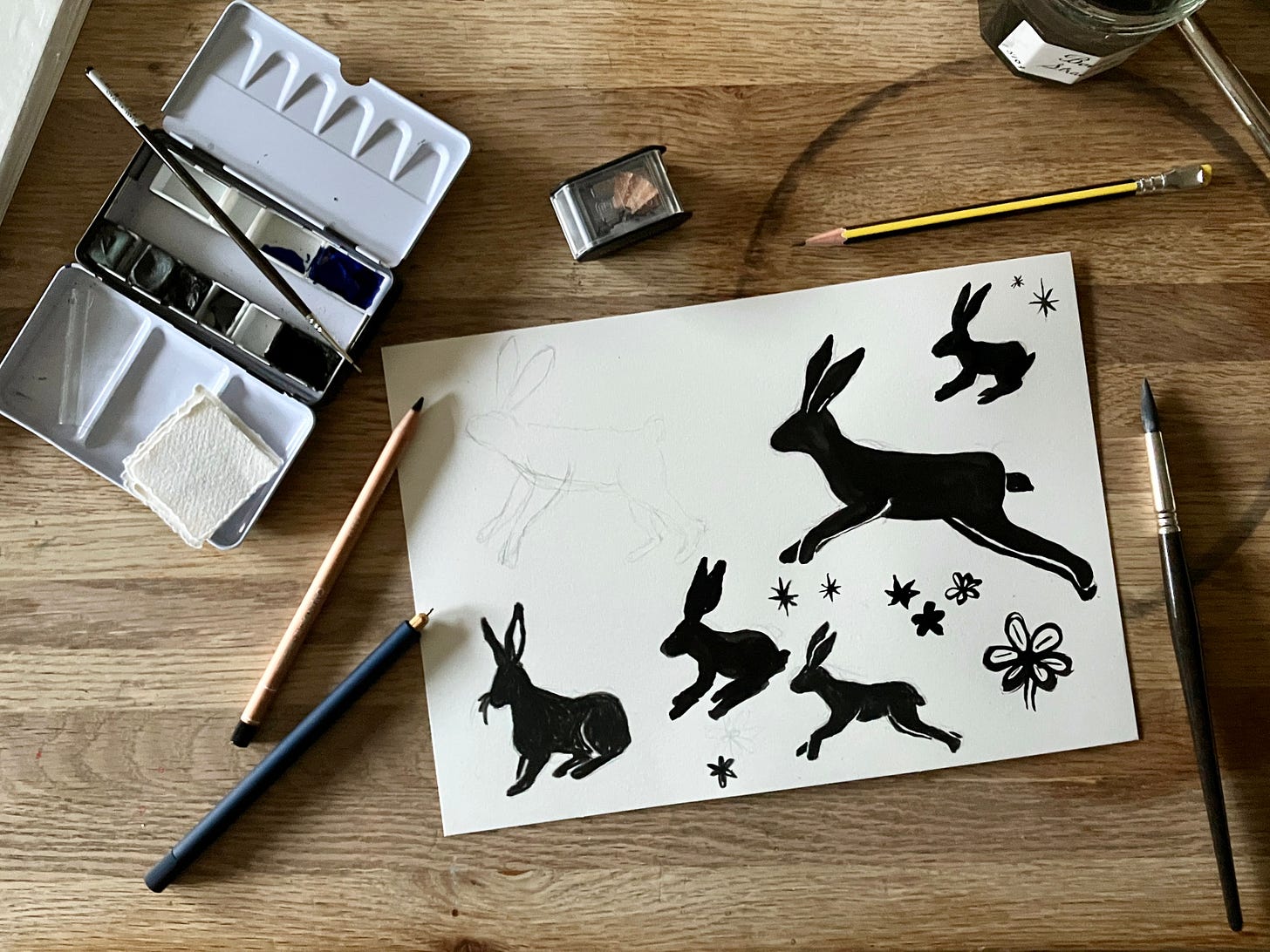 painting of hares sits atop a table surrounded by painting materials