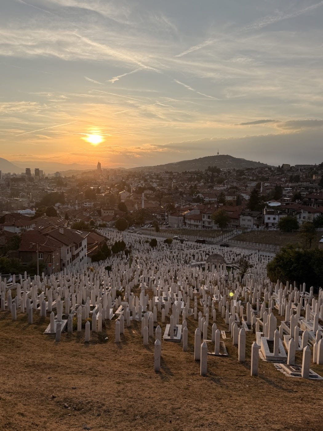 Sarajevo at sunset, with white cemetery headstones across the foreground. Photo by Amir.