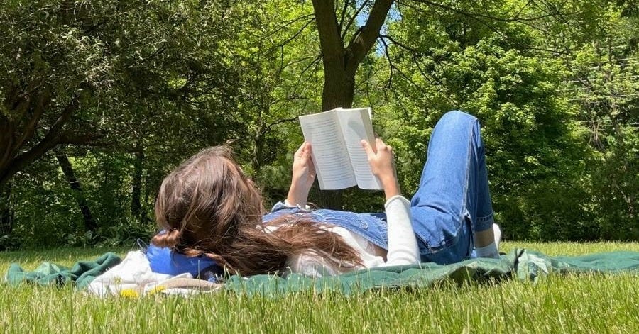 Woman sitting in blooming spring nature with a book, capturing the feeling of stepping away from Substack and finding balance