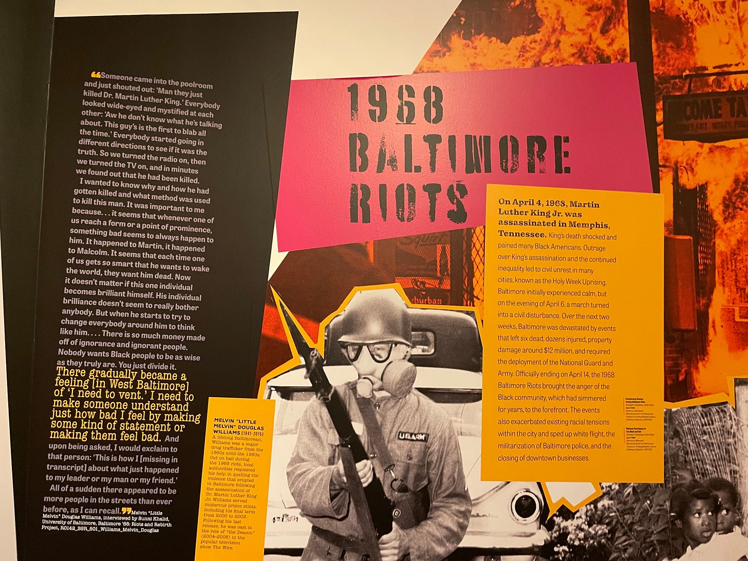 A series of museum display panels with the text heading “1968 BALTIMORE RIOTS.” Accompanying images include flaming buildings and a person dressed in riot gear. A series of museum display panels with the text heading “1968 BALTIMORE RIOTS.” Accompanying images include flaming buildings and a person dressed in riot gear.