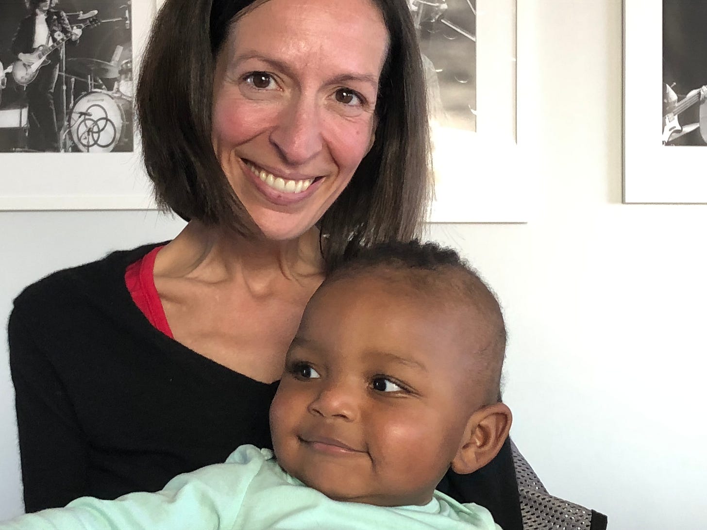 A white woman with brown hair holds a Black baby on her lap and grins. 