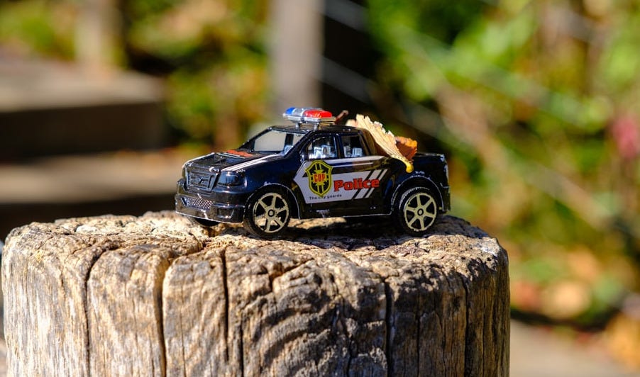 Toy police car sits on a weathered wooden post.