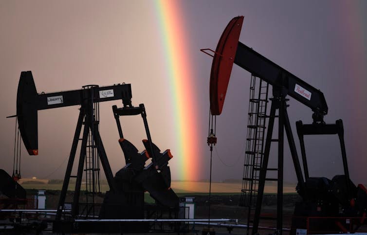 Pumpjacks seen against a dark, purplish sky split in half by a rainbow