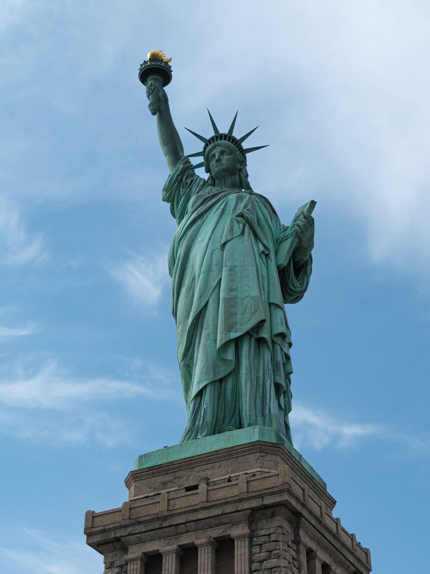 Looking up at the statue of liberty in New York Harbor. The green copper patina set against blue skies.  
