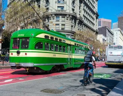 Bright green vintage streetcar and cyclist on Market Street in San Francisco, California.