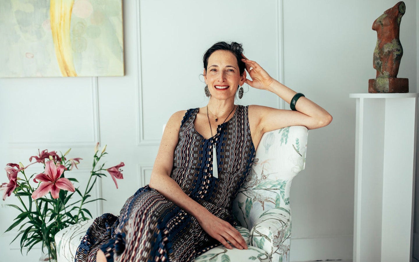 Dr. Catherine Price sitting on a chair in studio with flowers and a painting in the background Dr. Catherine Price sitting on a chair in studio with flowers and a painting in the background
