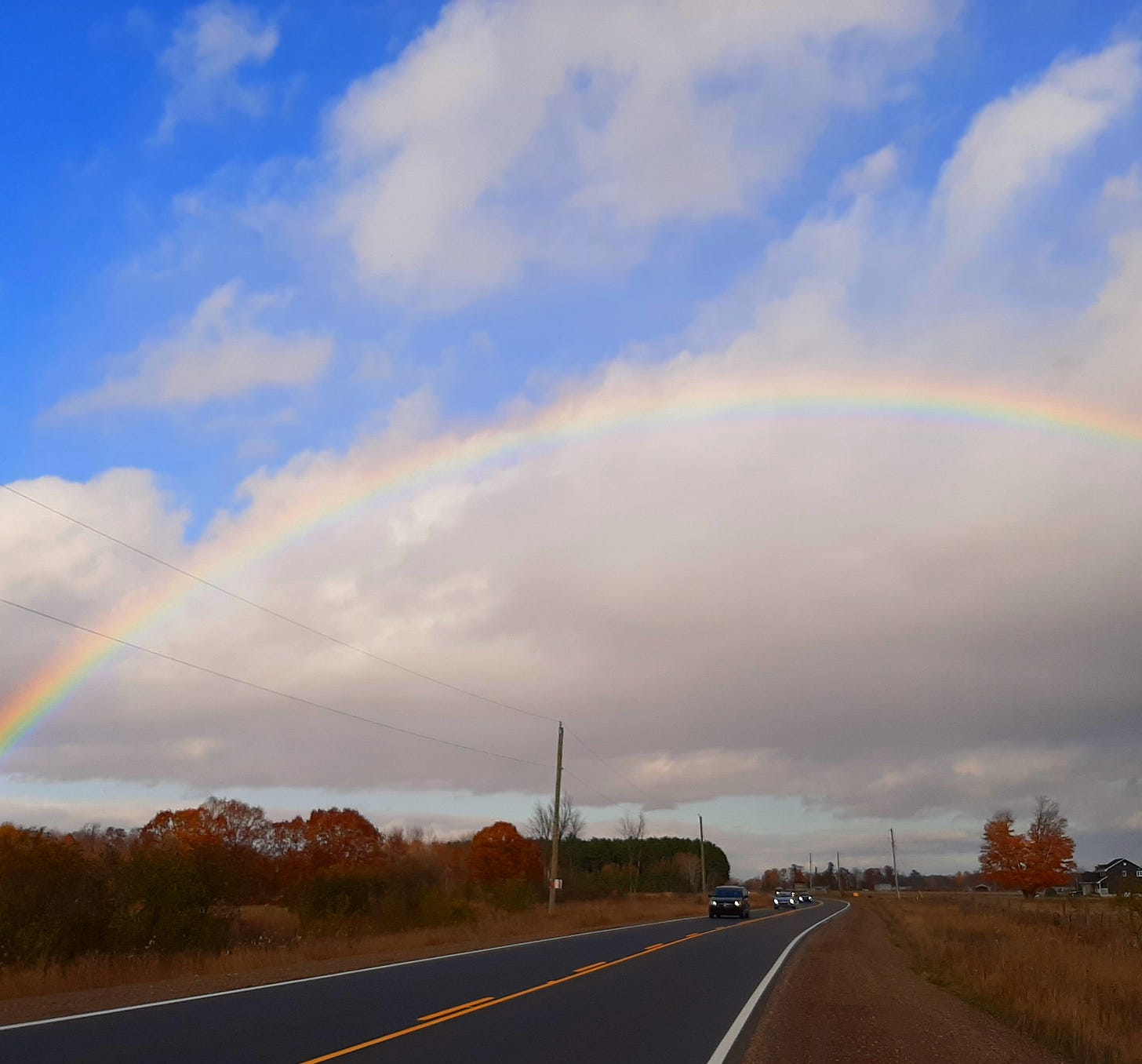 Photo of a full rainbow over a highway, clear road ahead
