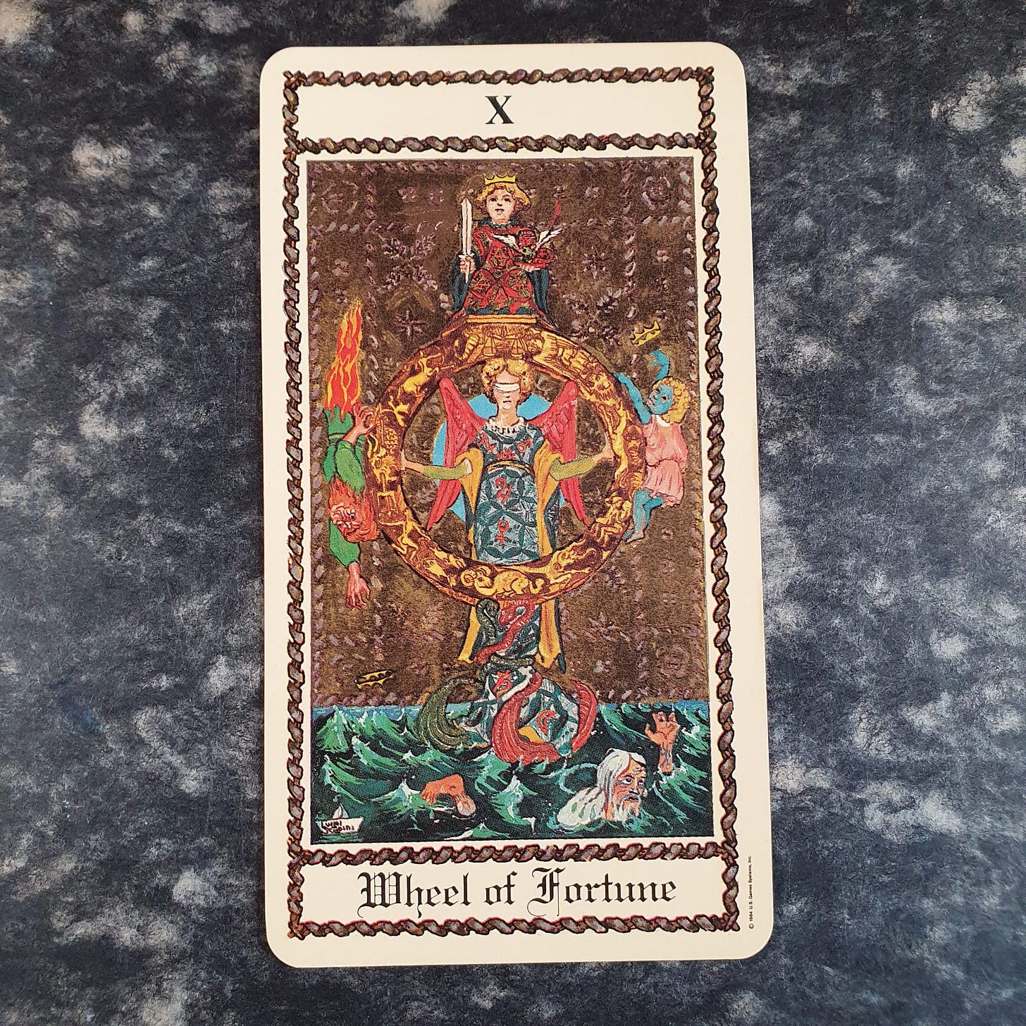 The Wheel of Fortune tarot card, numbered X, showing crowned and monstrous figures arranged around a large golden wheel above rough water.https://cardmeanings.com/cards/wheel-of-fortune/ The Wheel of Fortune tarot card, numbered X, showing crowned and monstrous figures arranged around a large golden wheel above rough water.https://cardmeanings.com/cards/wheel-of-fortune/