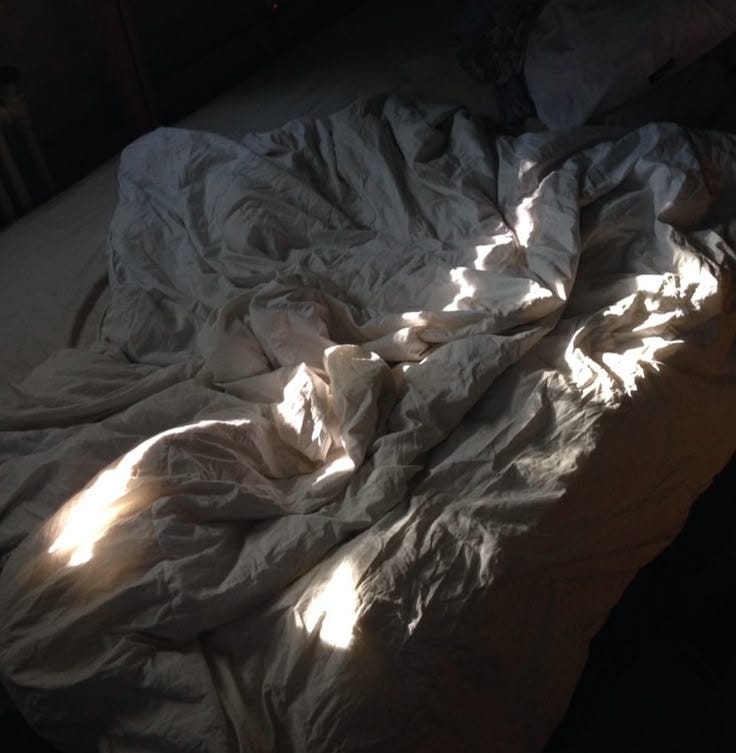 This may contain: an unmade bed with white sheets and sunlight coming through the window on top of it
