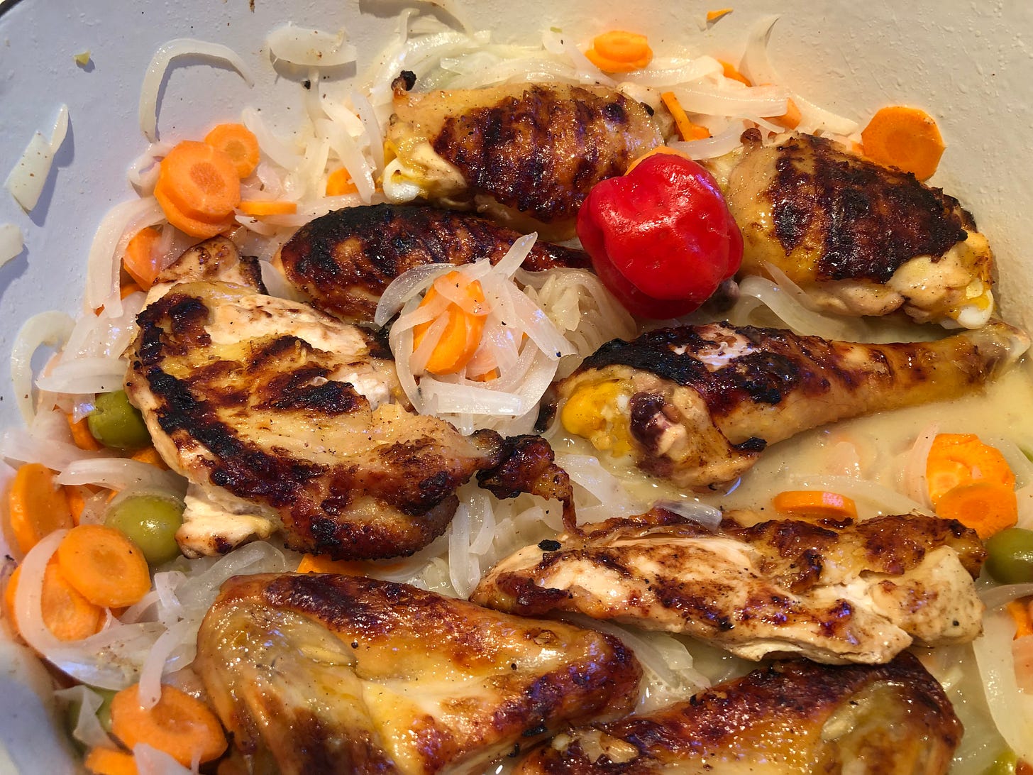 Grilled chicken pieces simmering in a dutch oven with onion, carrots, olives and marinade. 