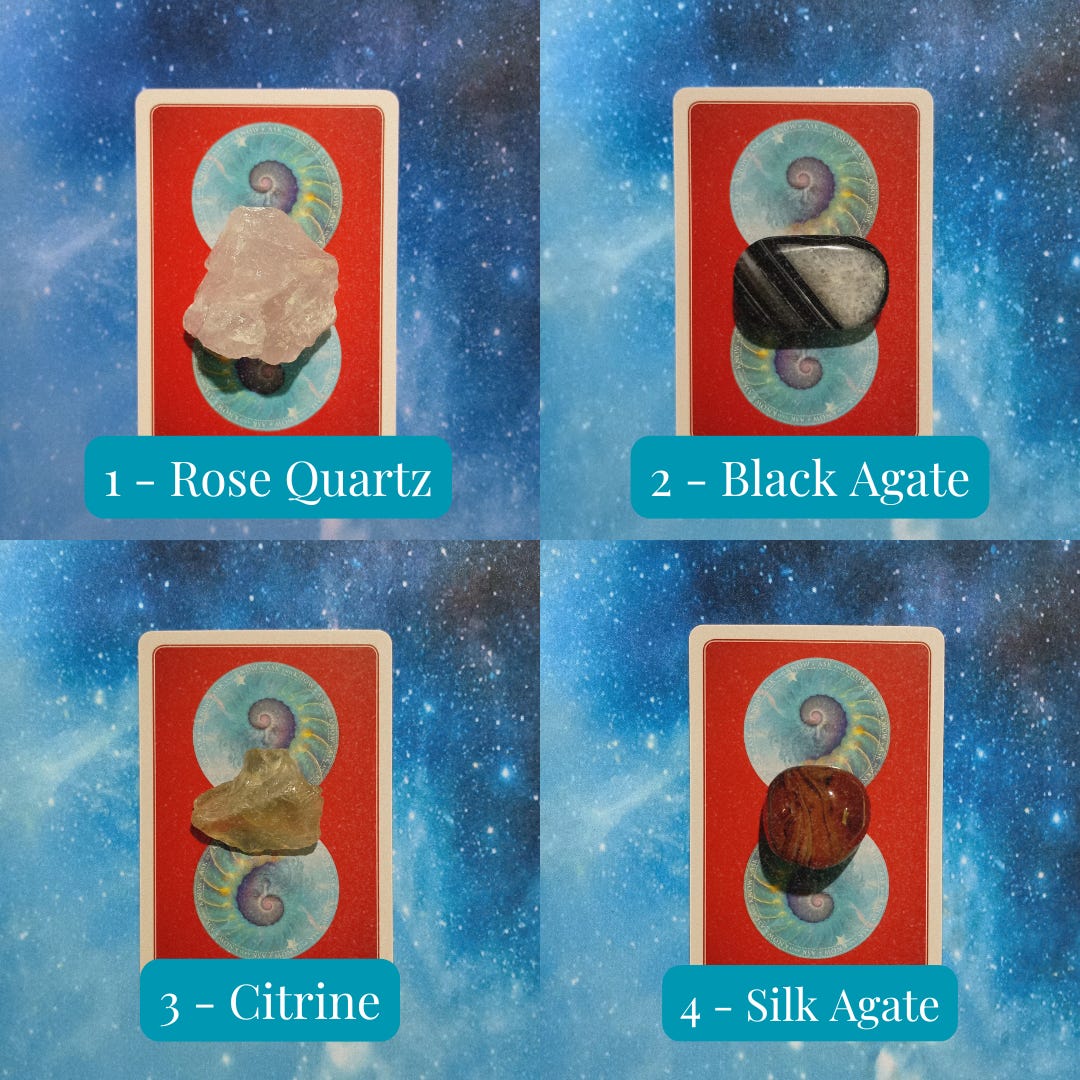 Crystals and face-down cards on a starry blue background. Pile 1 - Rose Quartz (pink), Pile 2 - Black Agate, Pile 3 - Citrine (yellow), Pile 4 - Silk Agate (red and brown)