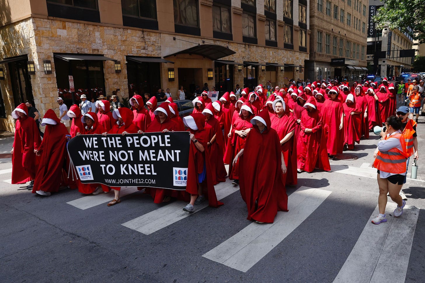 Dozens of women dressed as handmaidens from the show  The Handmaid s Tale  walk silently...