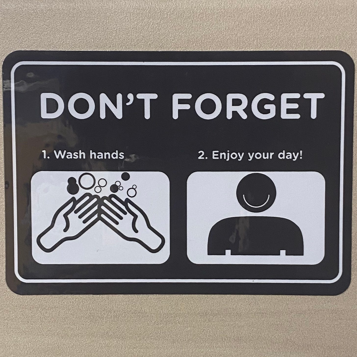 A sign that reads "Don't forget: 1. Wash hands 2. Enjoy your day!" with an image of two hands with bubbles and a smiling face.