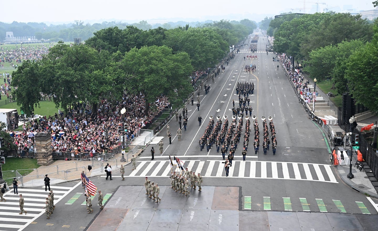 picture of military troops marching down street with medium sized crowd on the left and minimal crowd on the right