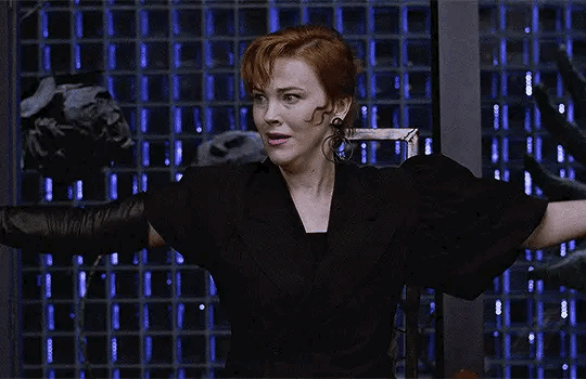 This may contain: a woman with red hair and black dress holding her arms out in front of the camera
