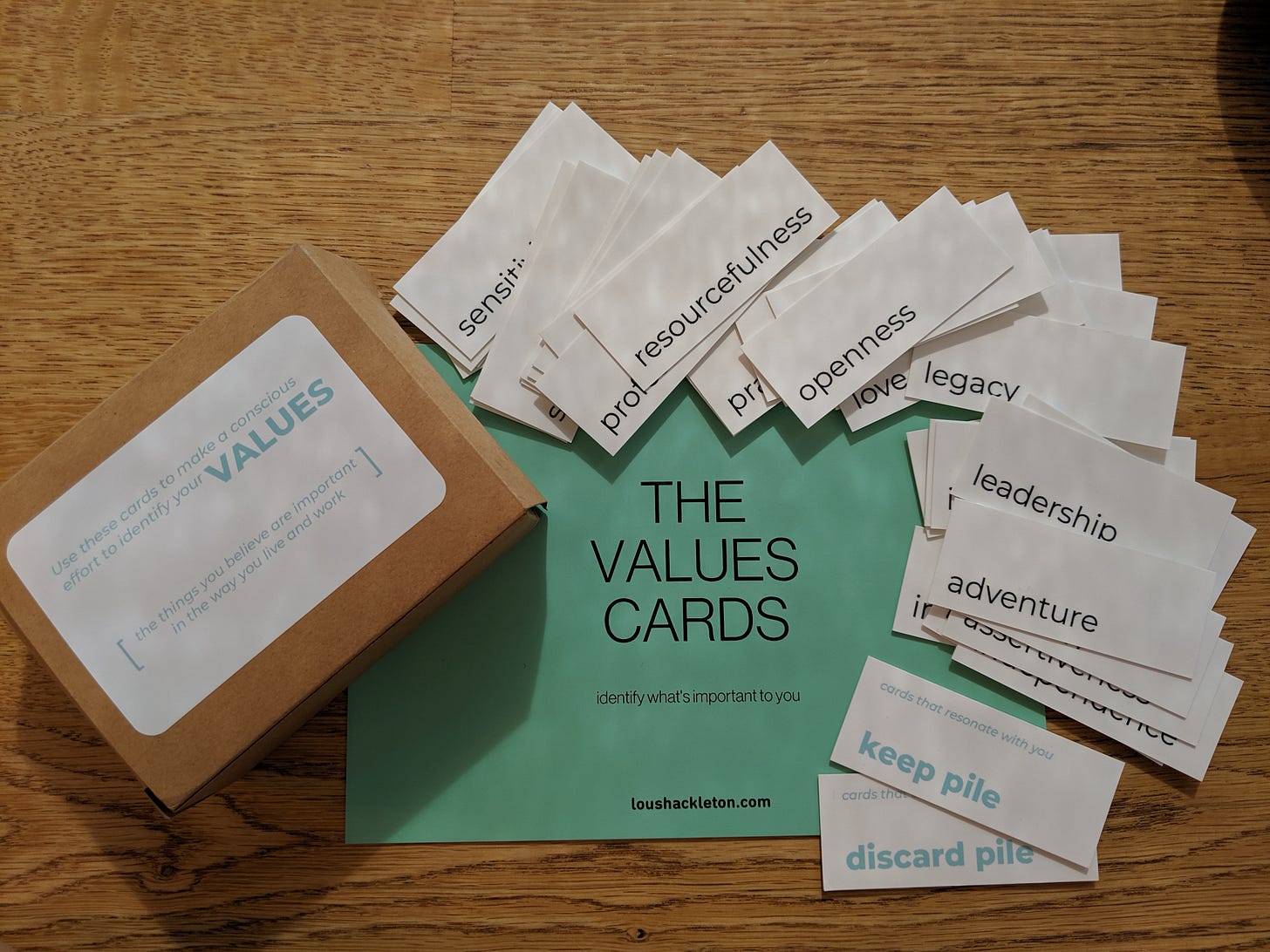 Image shows a set of cards on a table top. There is a box to the left with a sticker on it which reads, ‘Use these cards to make a conscious effort to identify your values. The things you believe are important in the way you live and work.’ In the centre there is a large green postcard with the words ‘the values cards’ and ‘identify what’s important to you.’ Fanned around the top and the right are small cards, each with a single word on - like resourcefulness, openness, legacy, leadership and adventure. Two of the small cards are at the bottom to the right - one reads ‘keep pile’ and the other reads ‘discard pile.’