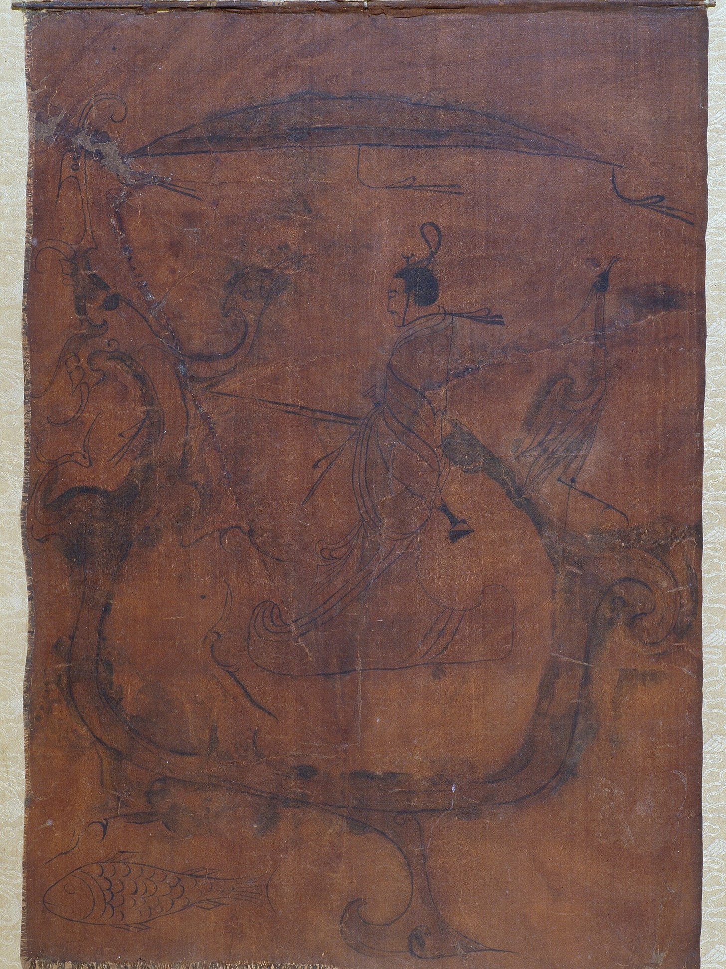 On a dark brown silk, a bearded man in a long robe and tall hat stands in profile holding reins, riding a long dragon shaped like a boat, under a canopy, with a bird on the dragon's tail and a fish swimming below. On a dark brown silk, a bearded man in a long robe and tall hat stands in profile holding reins, riding a long dragon shaped like a boat, under a canopy, with a bird on the dragon's tail and a fish swimming below.