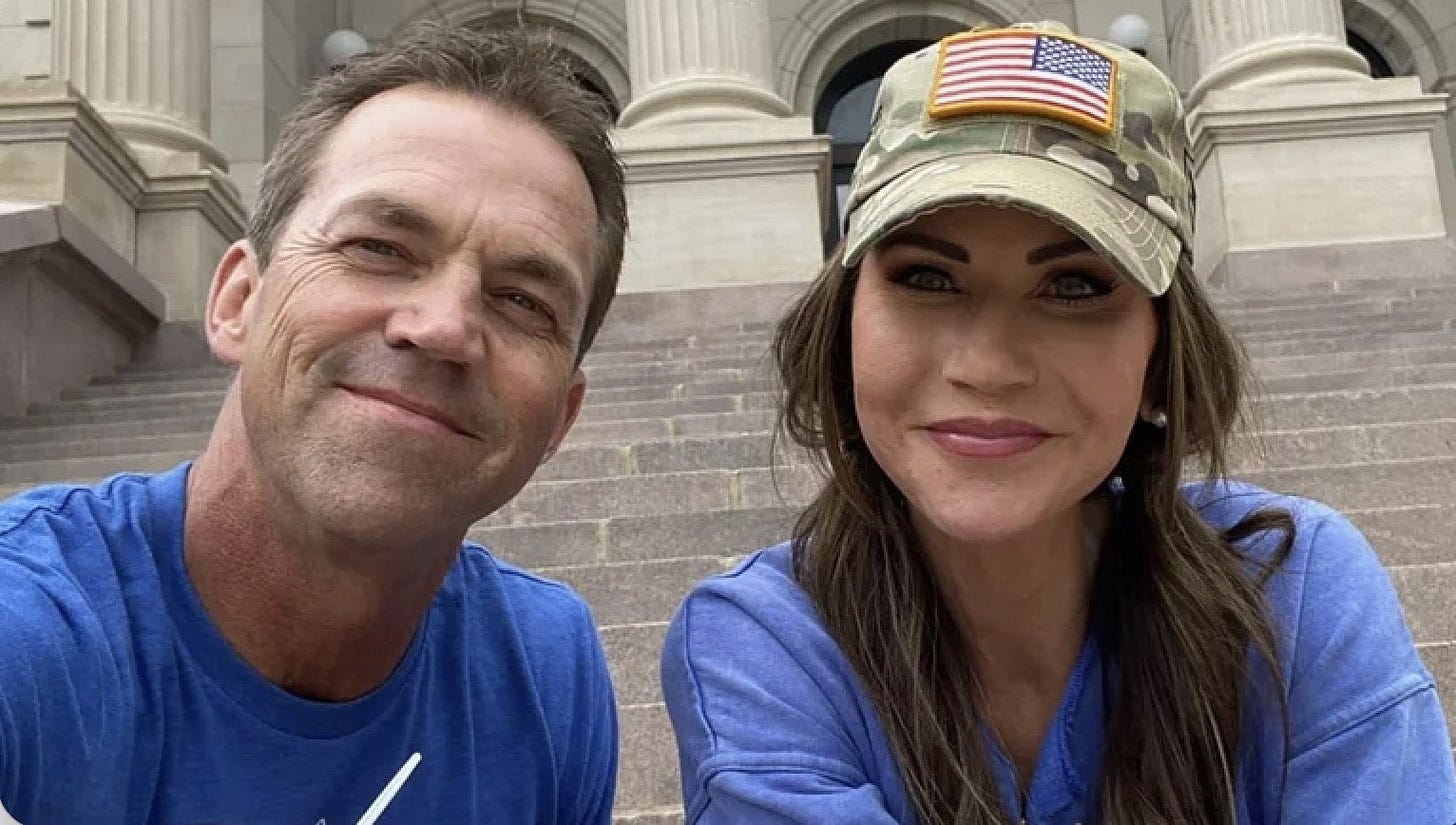 Smiling couple posing for a selfie on outdoor steps, wearing casual blue shirts and a camo hat with an American flag patch. Smiling couple posing for a selfie on outdoor steps, wearing casual blue shirts and a camo hat with an American flag patch.