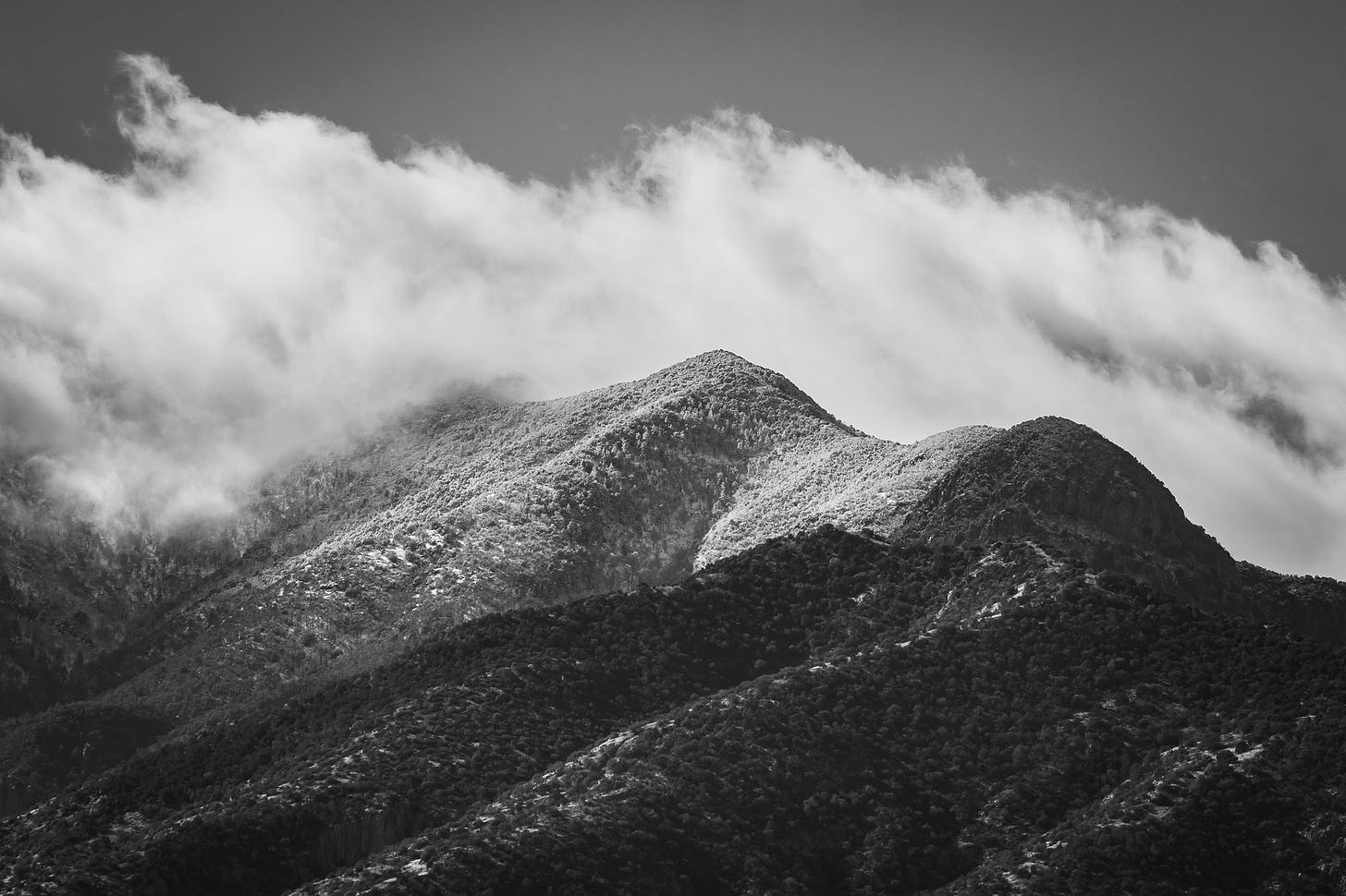 Fresh snow on a mountain top with whisky low clouds partially obscuring the peak.