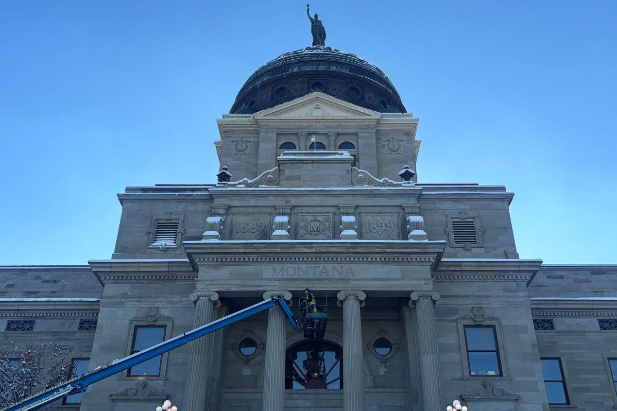 A photo of Montana's capitol with a few inches of snow. A construction worker in the foreground works on the building from a cherry-picker basket. A photo of Montana's capitol with a few inches of snow. A construction worker in the foreground works on the building from a cherry-picker basket.