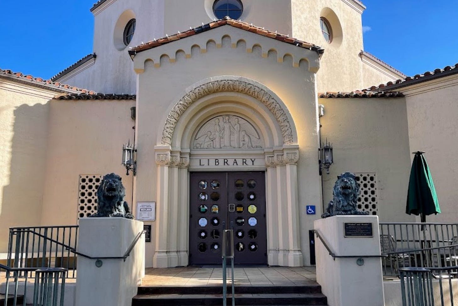 The outside of a library in adobe style, off-white with a brown door.