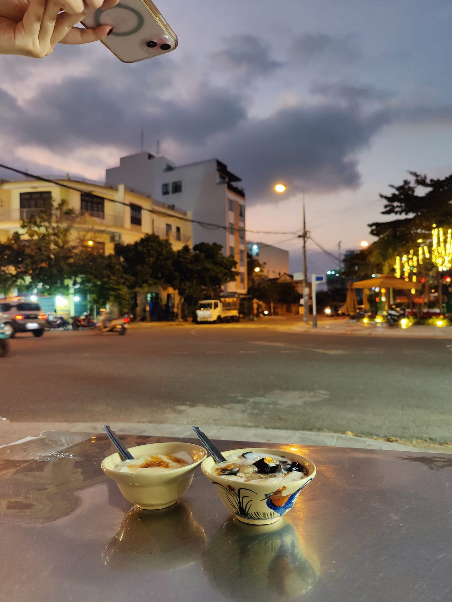 a friend takes a photo of a friend taking a photo of hot tofu pudding on a corner at dusk