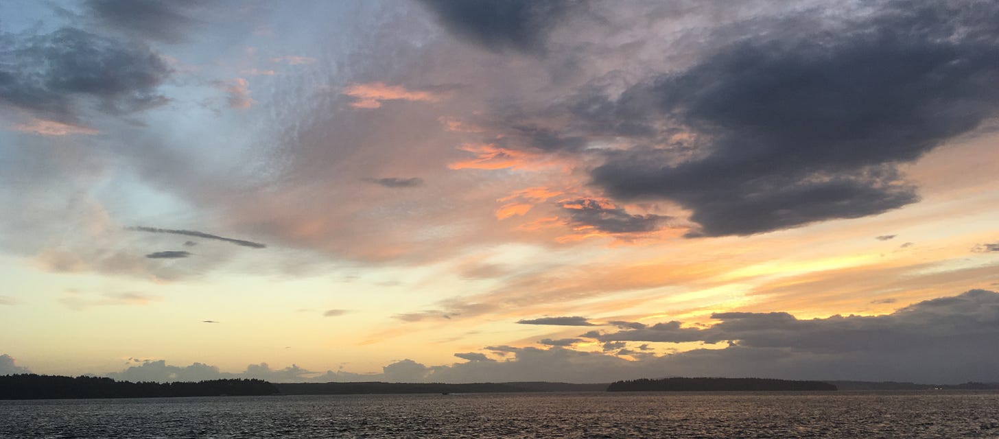 Cloudy sky at sunset, pinks and blues and yellows over black water.