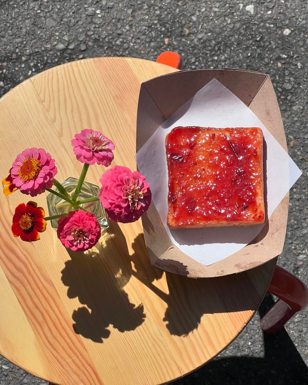 One slice of white shokupan bread with red jam on top of a wooden table, photographed from above