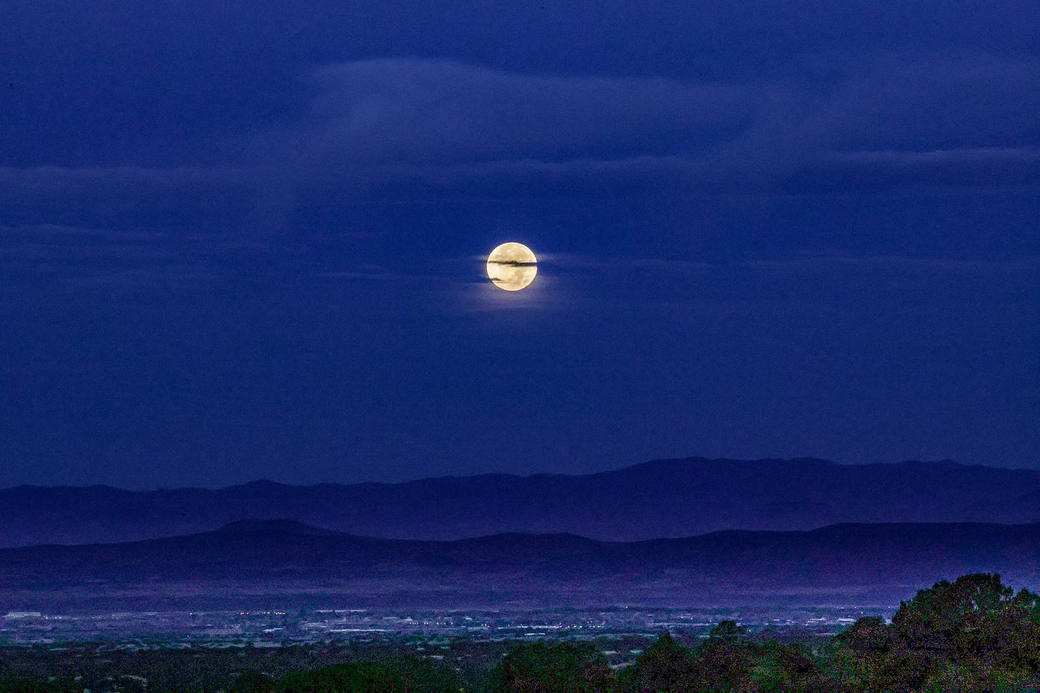 Full moon over a nighttime landscape with clouds and distant hills
