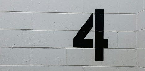 The number four painted in black on a grey wall.