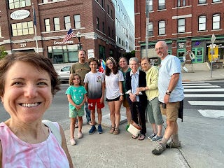 Me, smiling in the foreground, with my family (brother, mom, nieces, nephew, sister, brother-in-law, and mother-in-law) standing together in the background. We're on a street corner in small town Barre, Vermont. Me, smiling in the foreground, with my family (brother, mom, nieces, nephew, sister, brother-in-law, and mother-in-law) standing together in the background. We're on a street corner in small town Barre, Vermont.