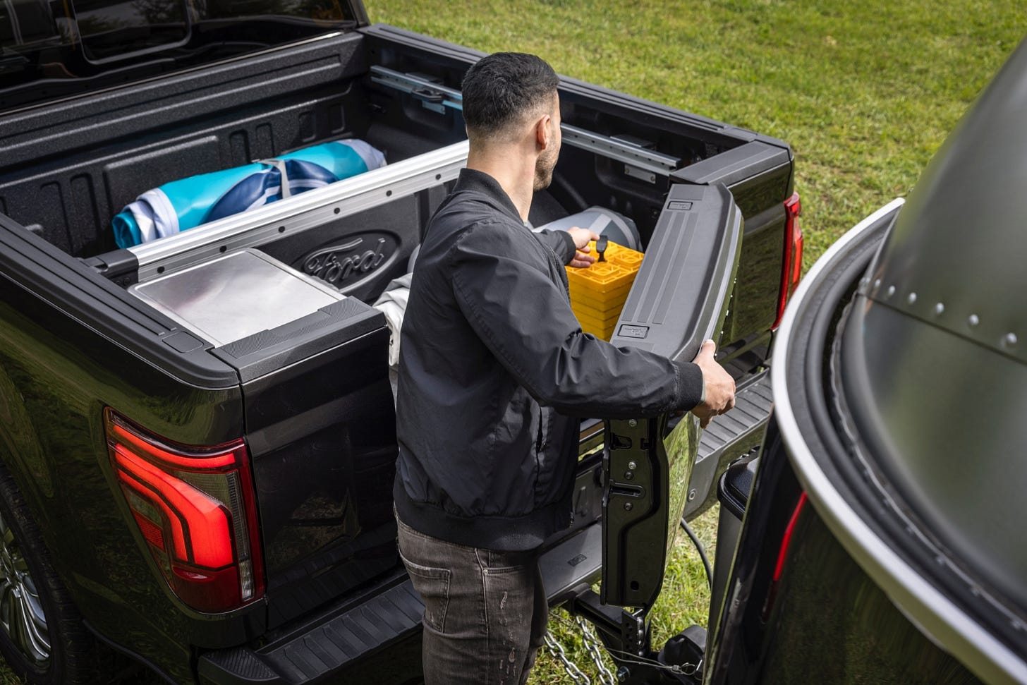 A man uses the Pro Access Tailgate on a 2024 Ford F-150 to reach items stored in the truck's cargo bed.