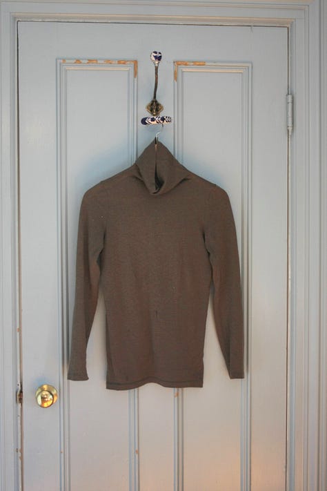 Five shirts, from left to right a white shirt, green turtleneck, oatmeal turtleneck, white t-shirt, and brown turtleneck