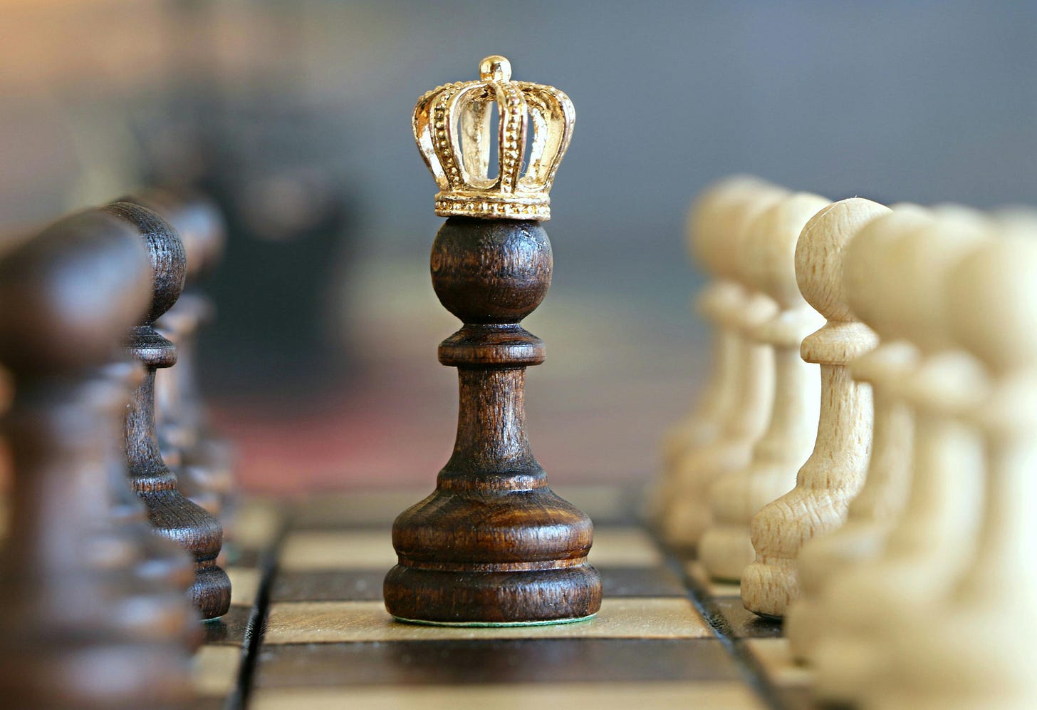 Black pawn with gold crown flanked on the left by a row of black pawns and on the right by a row of white pawns. Black pawn with gold crown flanked on the left by a row of black pawns and on the right by a row of white pawns.