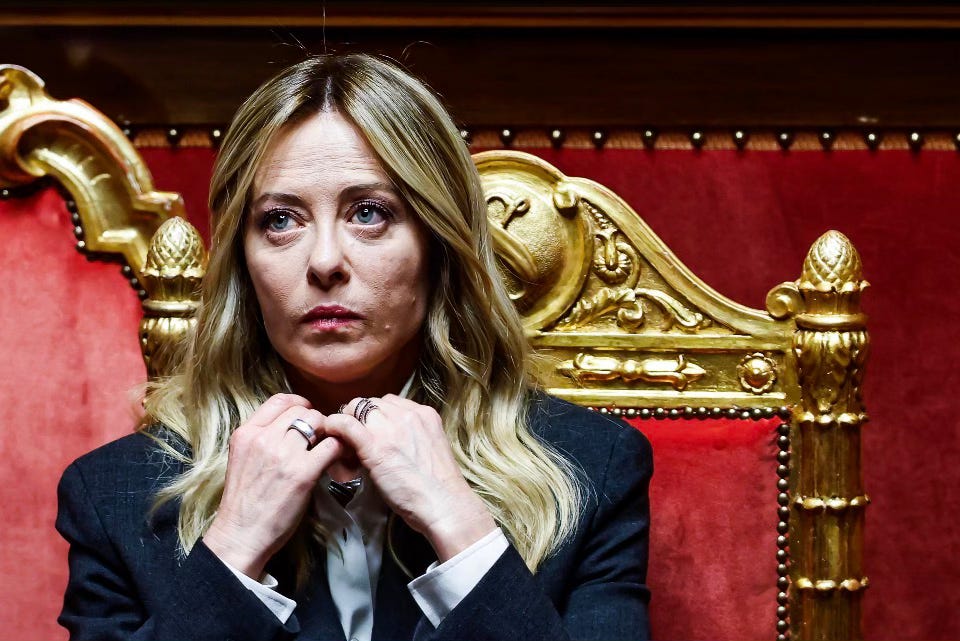 Giorgia Meloni seduta in aula parlamentare con sfondo dorato, sguardo teso. Giorgia Meloni seduta in aula parlamentare con sfondo dorato, sguardo teso.