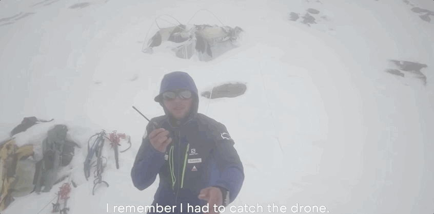 man catching a drone on top of a mountain