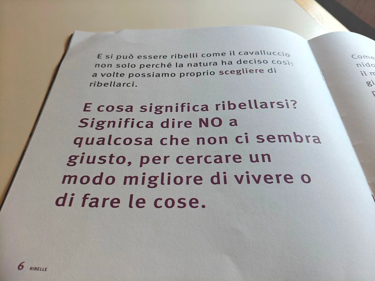 Una pagina della parola RIBELLE delle Scatoline di effequ, con questa scritta: "e cosa significa ribellarsi? Significa dire NO qualcosa non ci sembra è giusto, per cercare il modo migliore di vivere o di fare le cose". La pagina è appoggiata su un tavolo di legno bianco sporco e nell'angolino in alto a destra si intravede un pezzetto di muro in ombra.