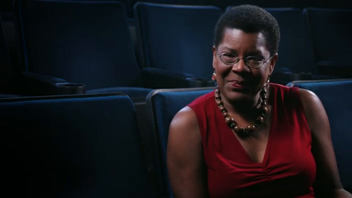 Black woman with red dress and short hair sits in a movie theater