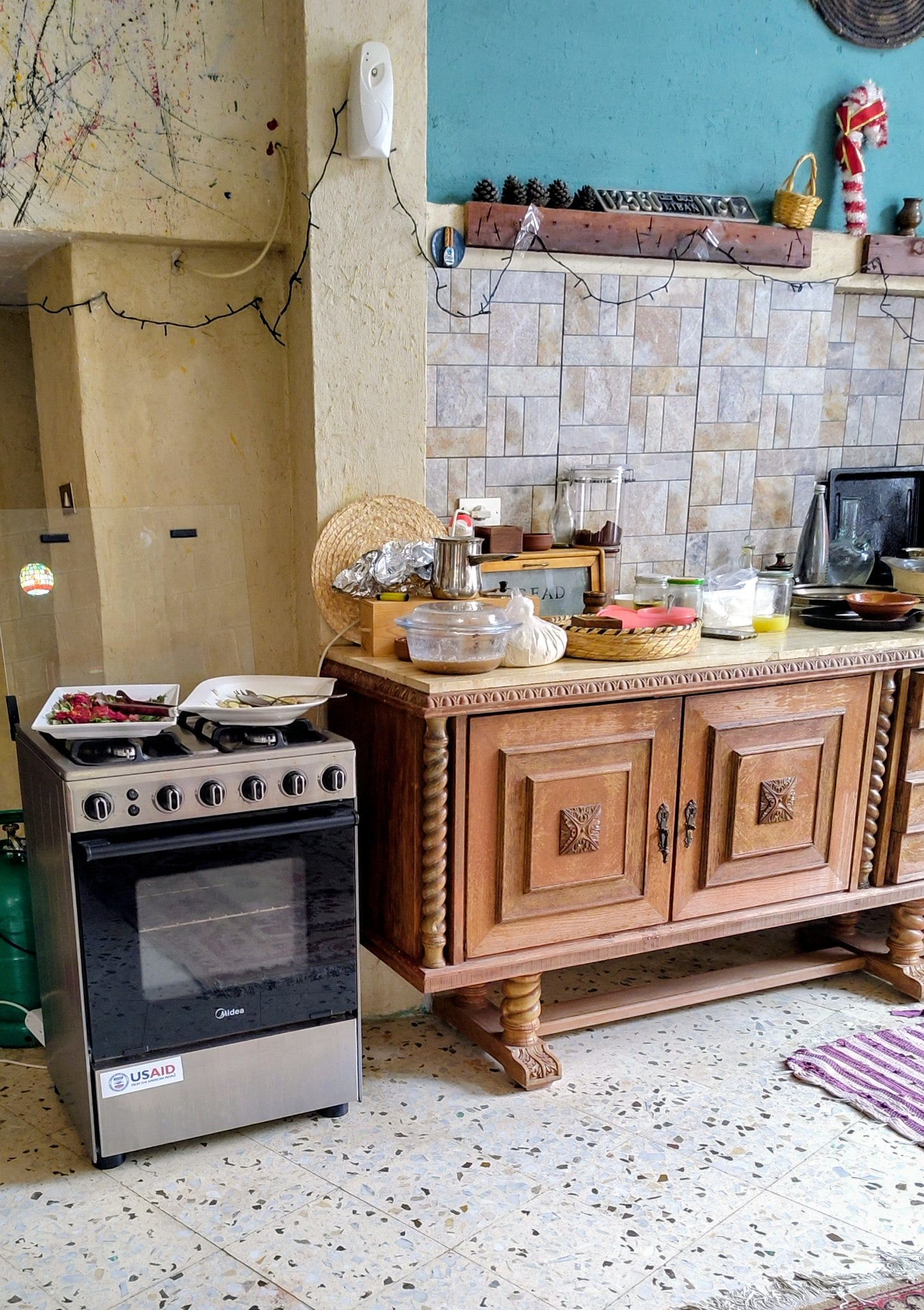 An open layout kitchen in a Lebanese guest house, with bowls and cooking utensils on the counter. Two plates of food rest on a stove that bears a USAID sticker. An open layout kitchen in a Lebanese guest house, with bowls and cooking utensils on the counter. Two plates of food rest on a stove that bears a USAID sticker.