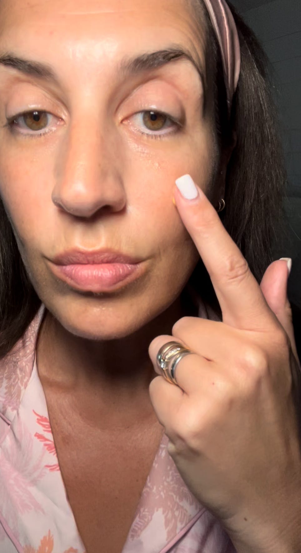 A close-up of a woman pointing to her cheekbone to demonstrate skincare product placement and skin texture.