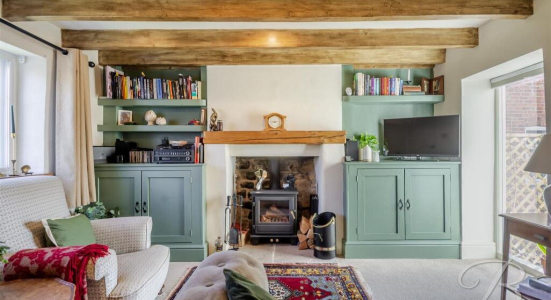 A living room with wooden beams, a wood-burning stove, and cream seats and carpet A living room with wooden beams, a wood-burning stove, and cream seats and carpet